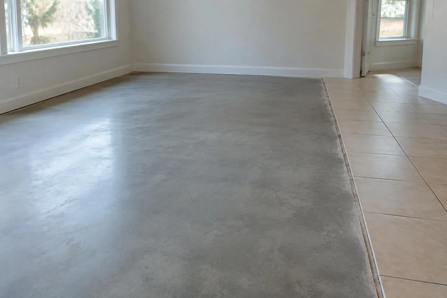 Exposed smooth concrete floor beside a remaining section of beige tile in an empty room
